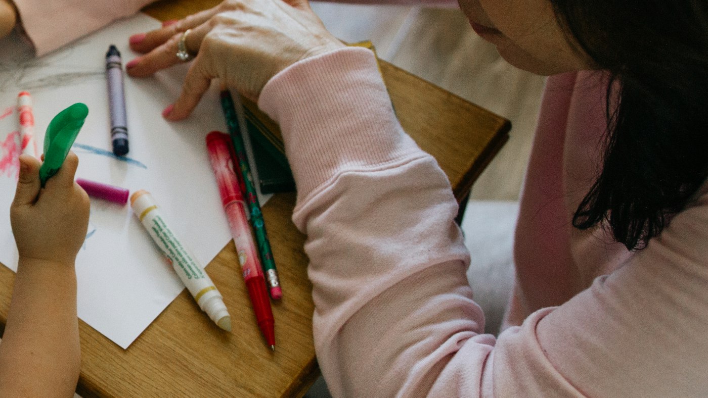 Des feutres posés sur une feuille, entre les mains d’un adulte et d’un enfant, sur une petite table en bois