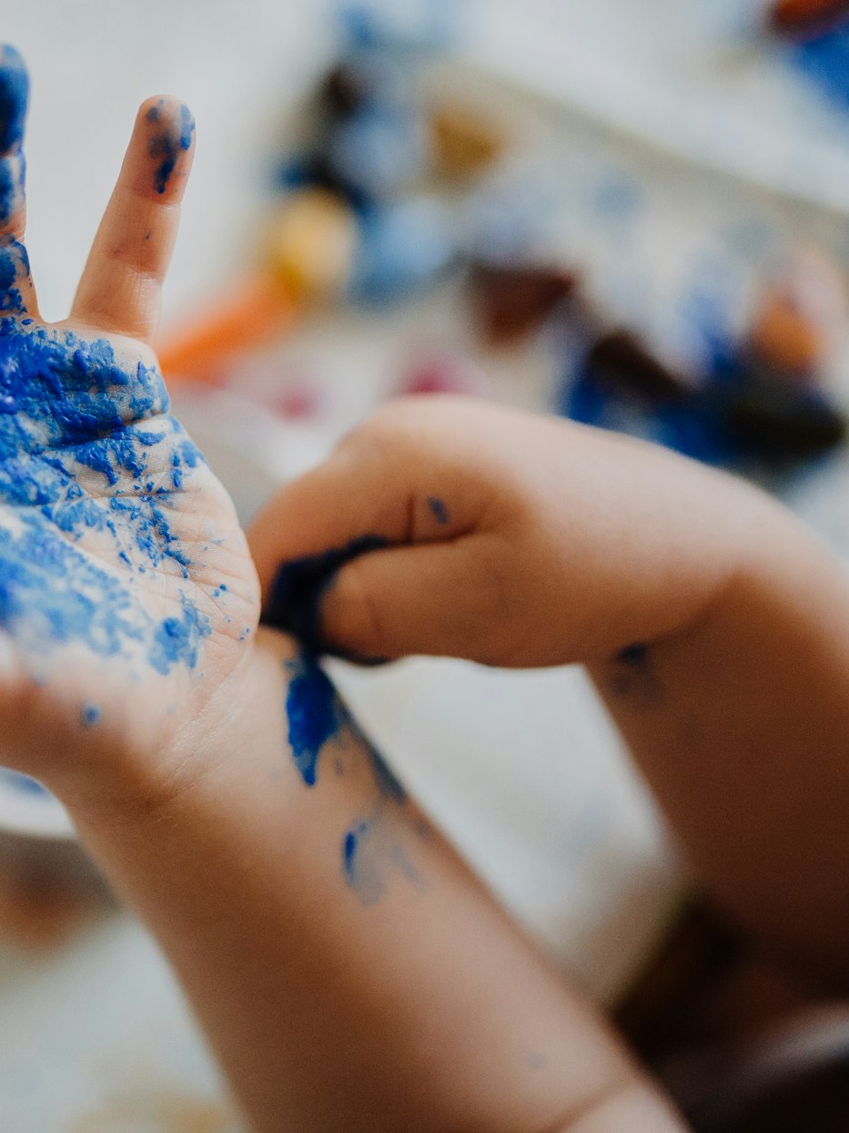 Une main d’enfant couverte de peinture bleue, posée sur une feuille