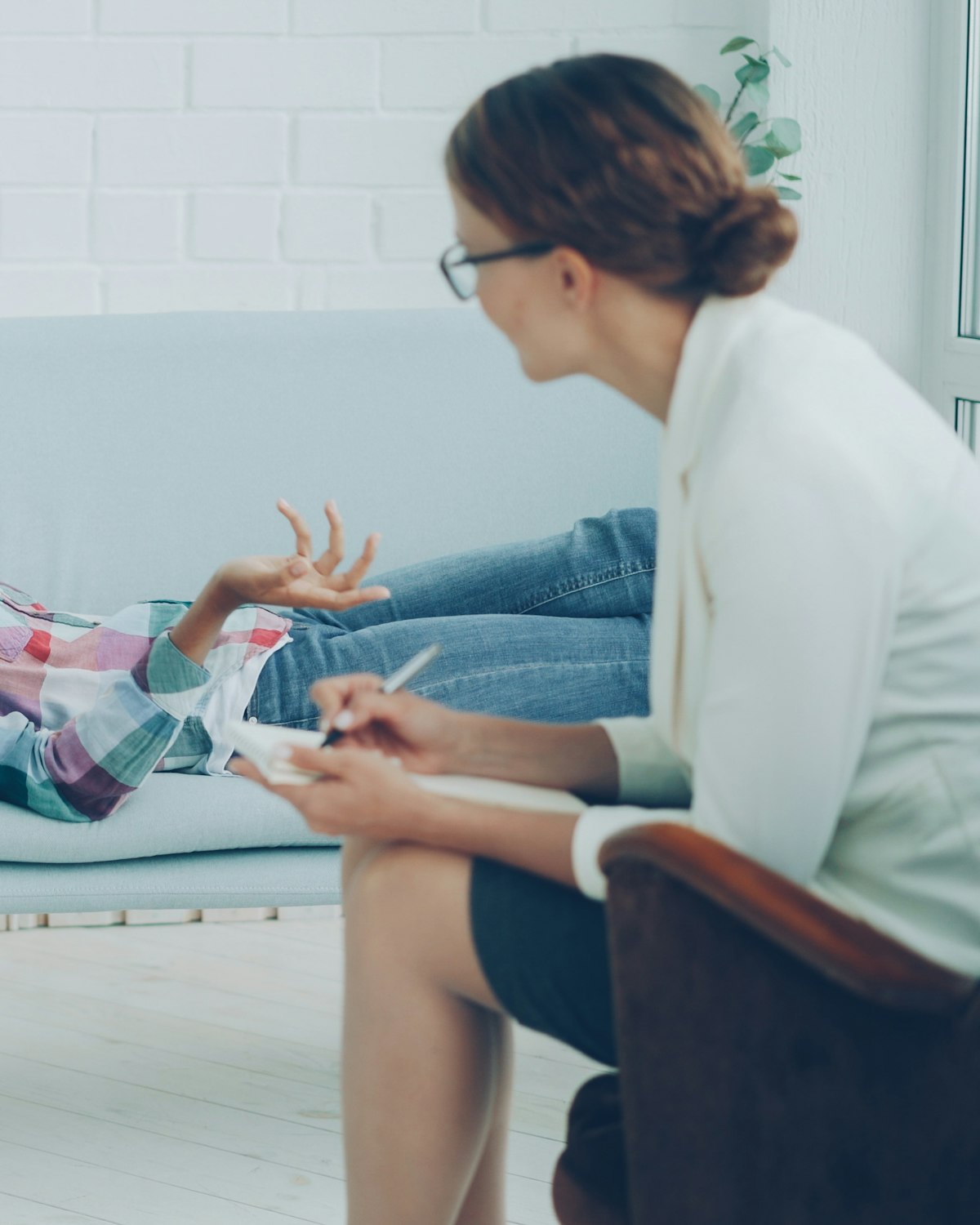 Une psychologue à l’écoute d’une jeune patiente allongée sur un canapé, dans une pièce claire